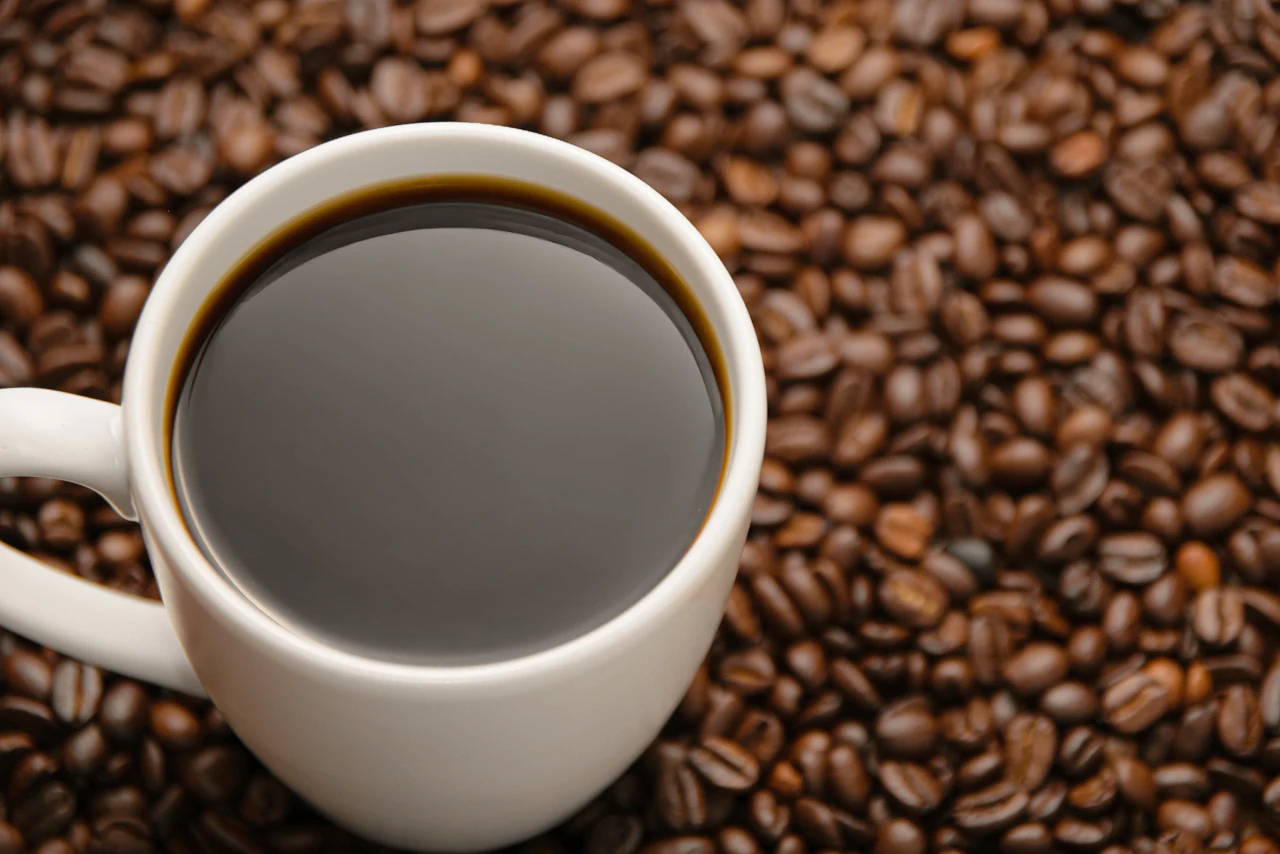 Taza blanca de café americano colocada sobre granos de café tostado