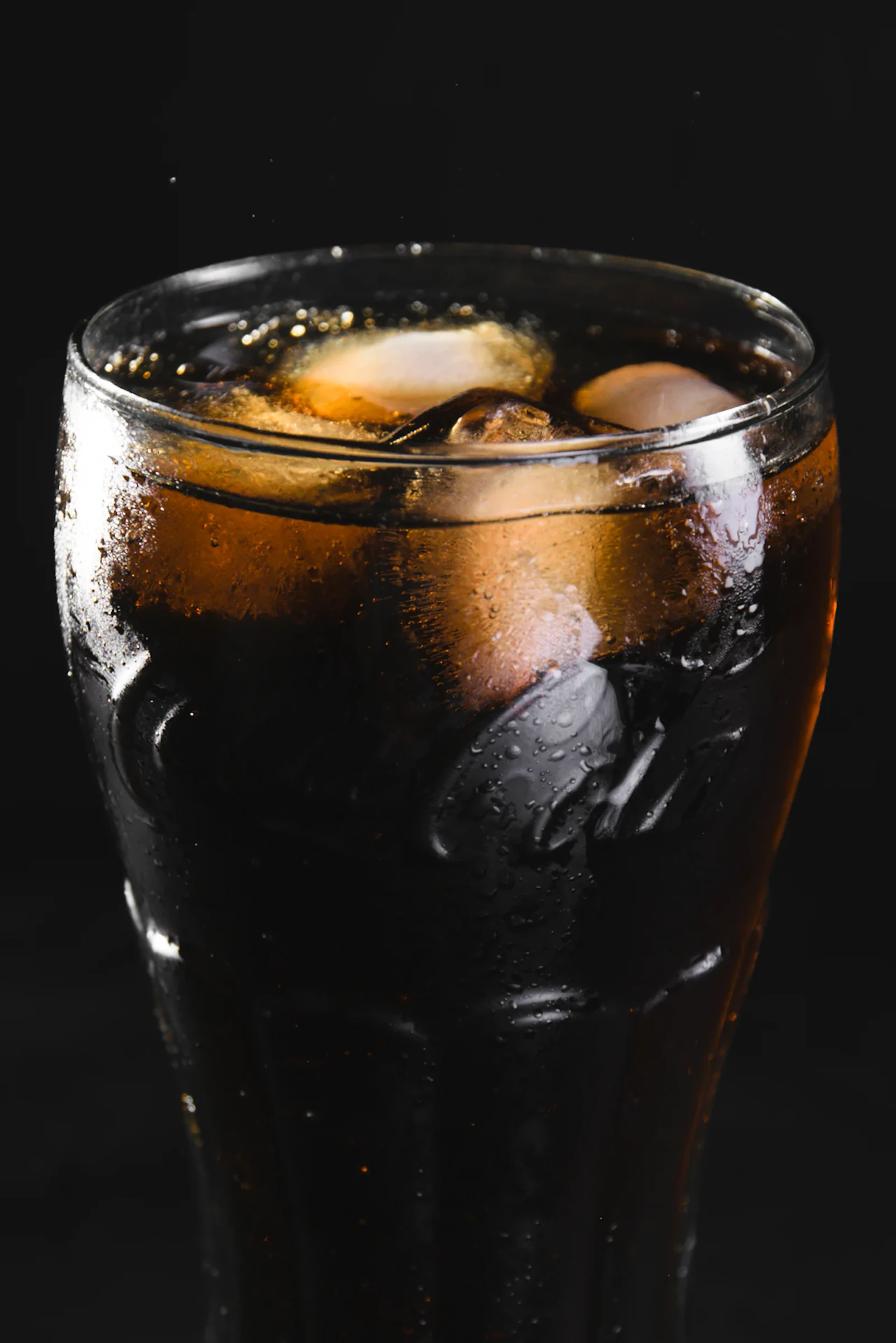Vaso de refresco de cola con hielos sobre fondo negro