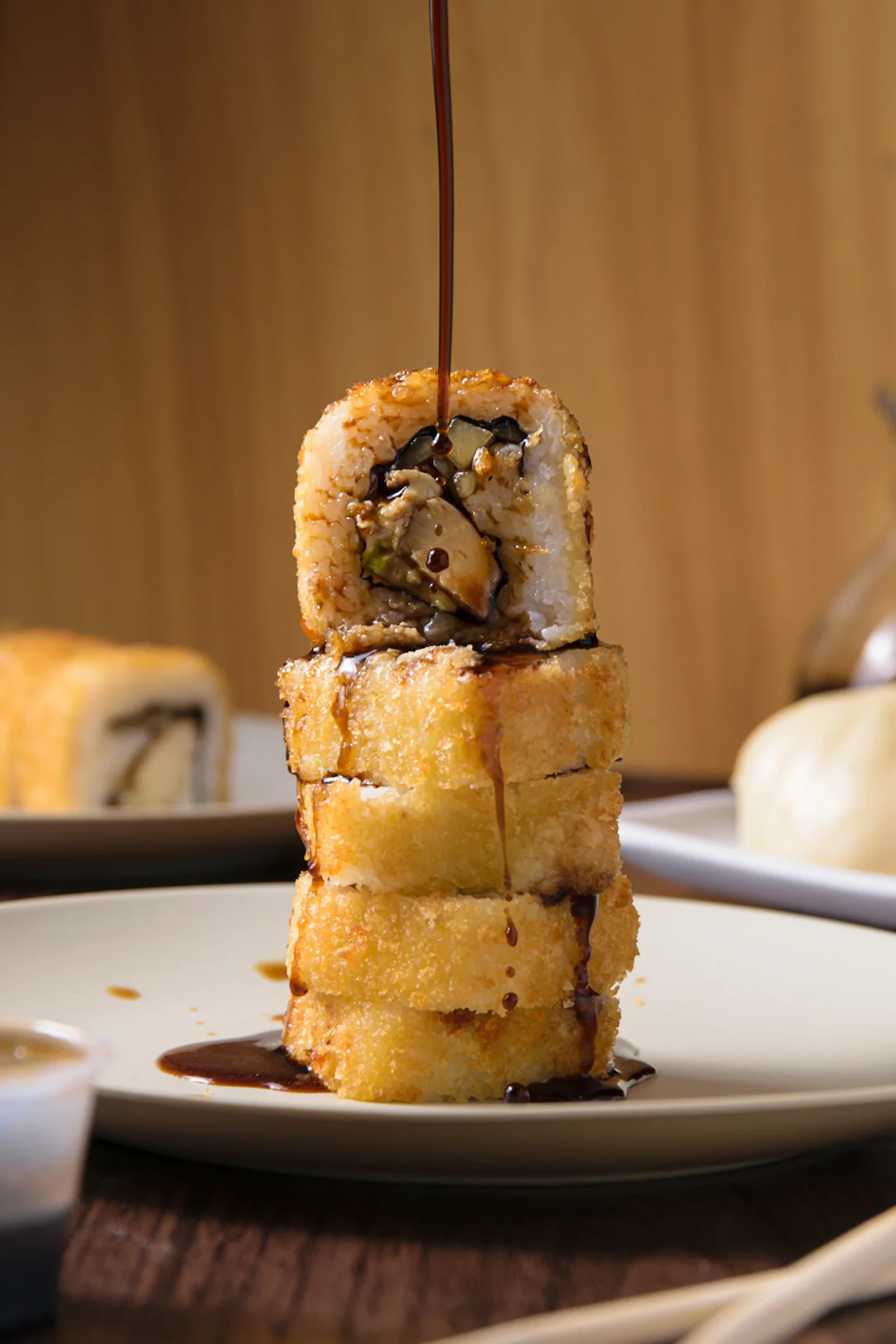 Torre de sushi empanizado bañada con salsa oscura sobre plato blanco