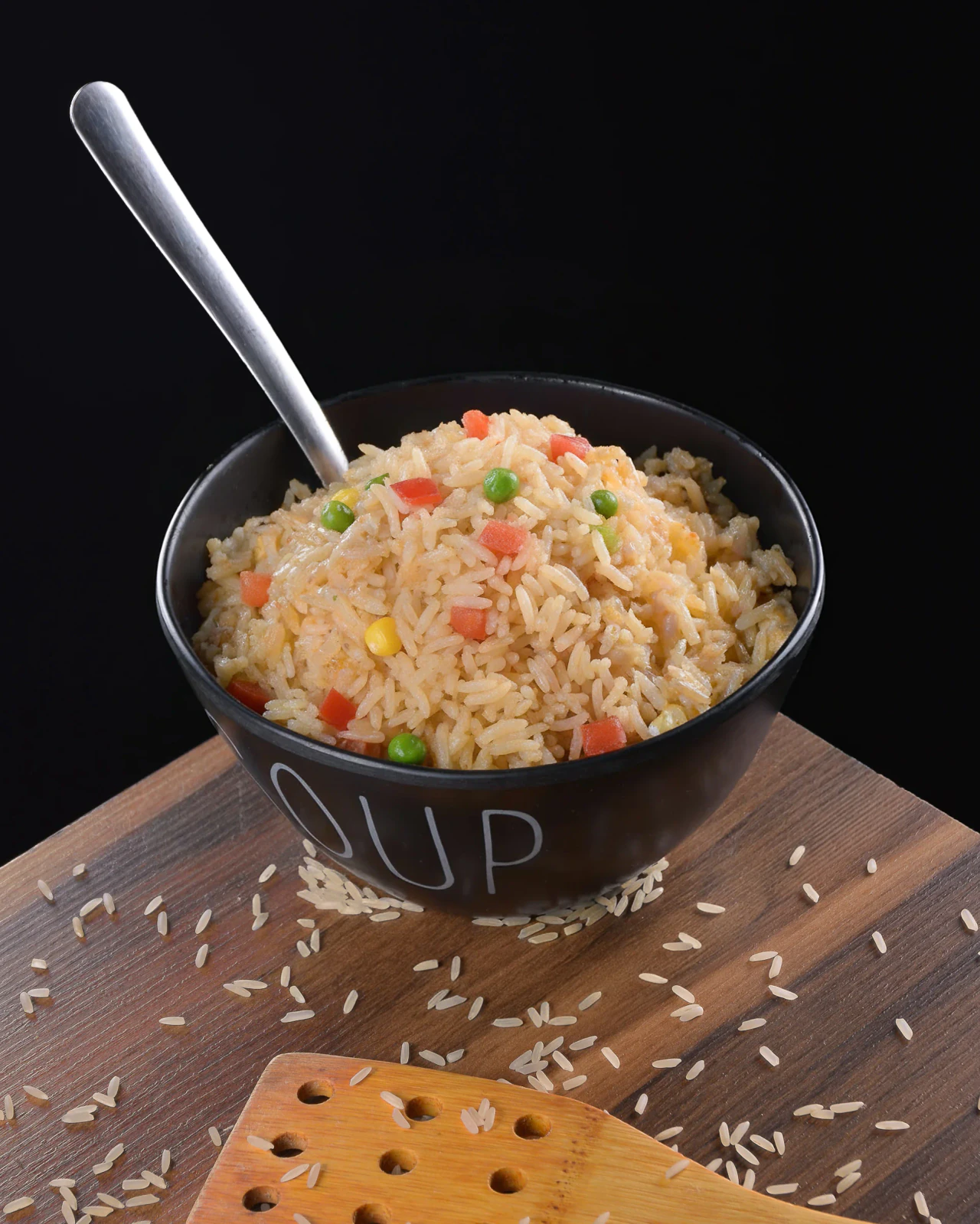 Arroz frito con verduras servido en bowl negro sobre tabla de madera