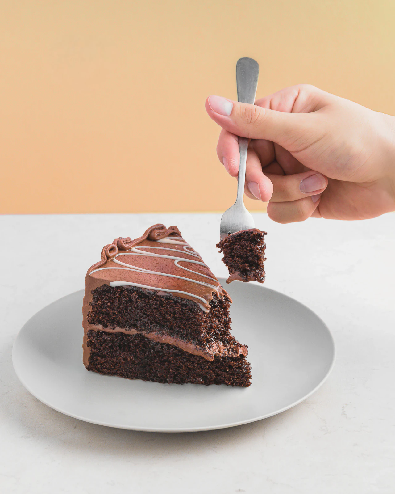 Rebanada de pastel de chocolate de dos capas en plato gris mientras una mano levanta un bocado con el tenedor